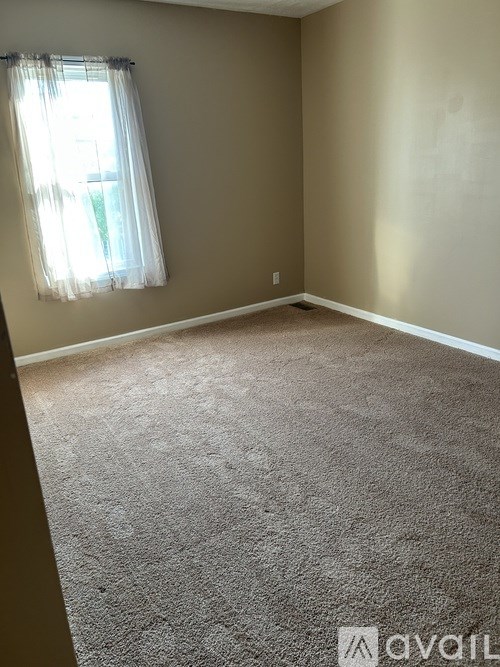 A room with a carpeted floor and a window with curtains.