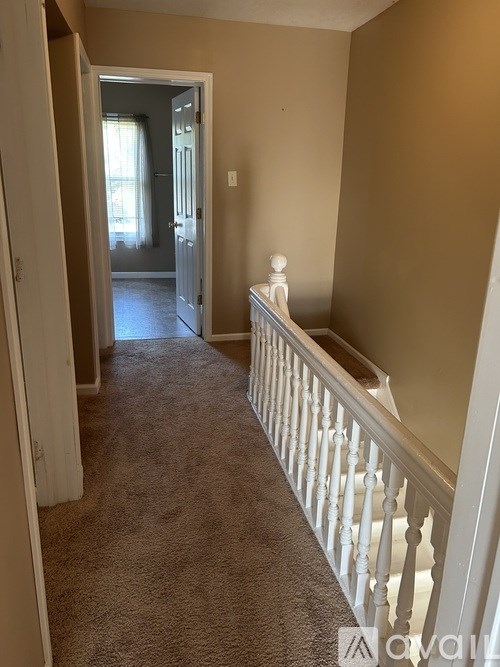 A hallway with a carpeted floor and a white railing.