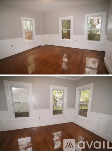 A room with wooden floors and white walls with three windows.
