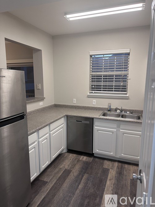 A kitchen with a stainless steel refrigerator, a window with blinds, and a sink with a faucet.