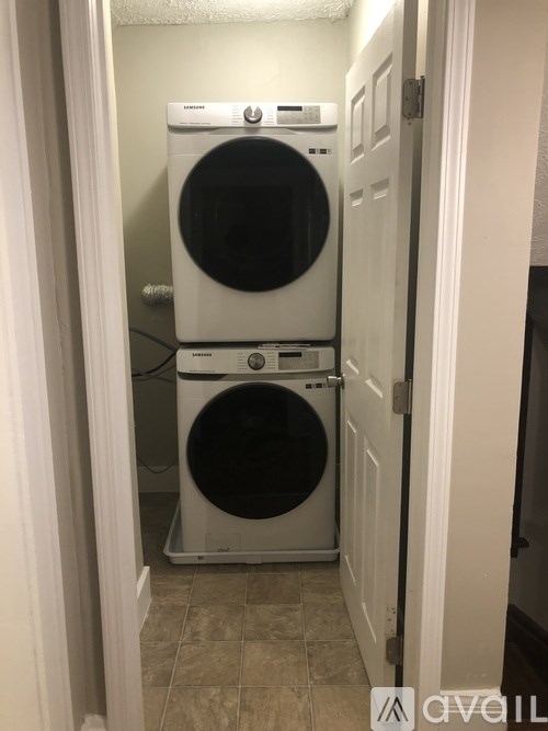 A white dryer and washer are stacked on top of each other in a small laundry room.