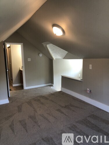 A carpeted room with a skylight and a doorway leading to another room.