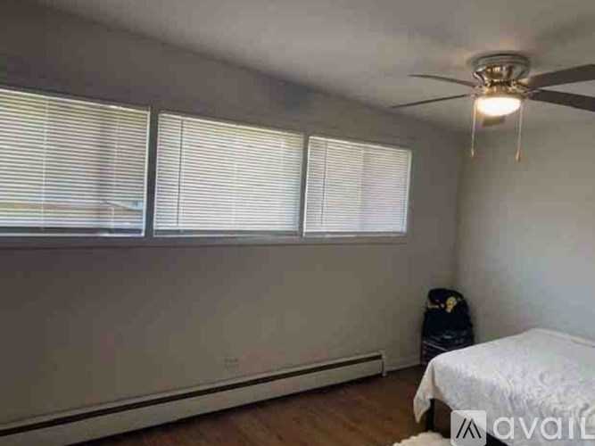 A room with a bed, a ceiling fan, and a window with blinds.