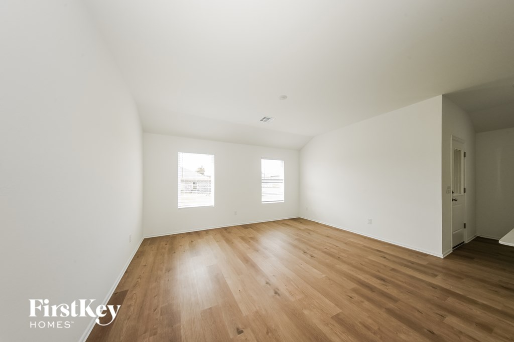 A room with wooden floors and white walls, with a window on the left wall.
