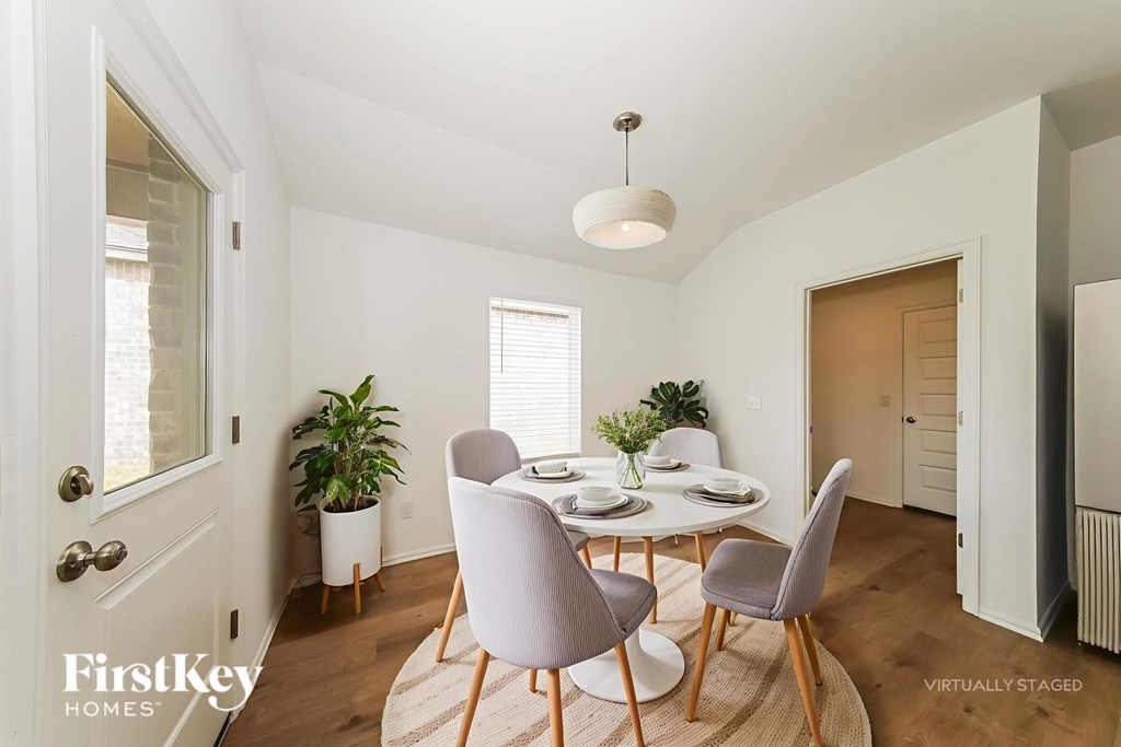 A dining room with a table set for two and a potted plant on the side table.