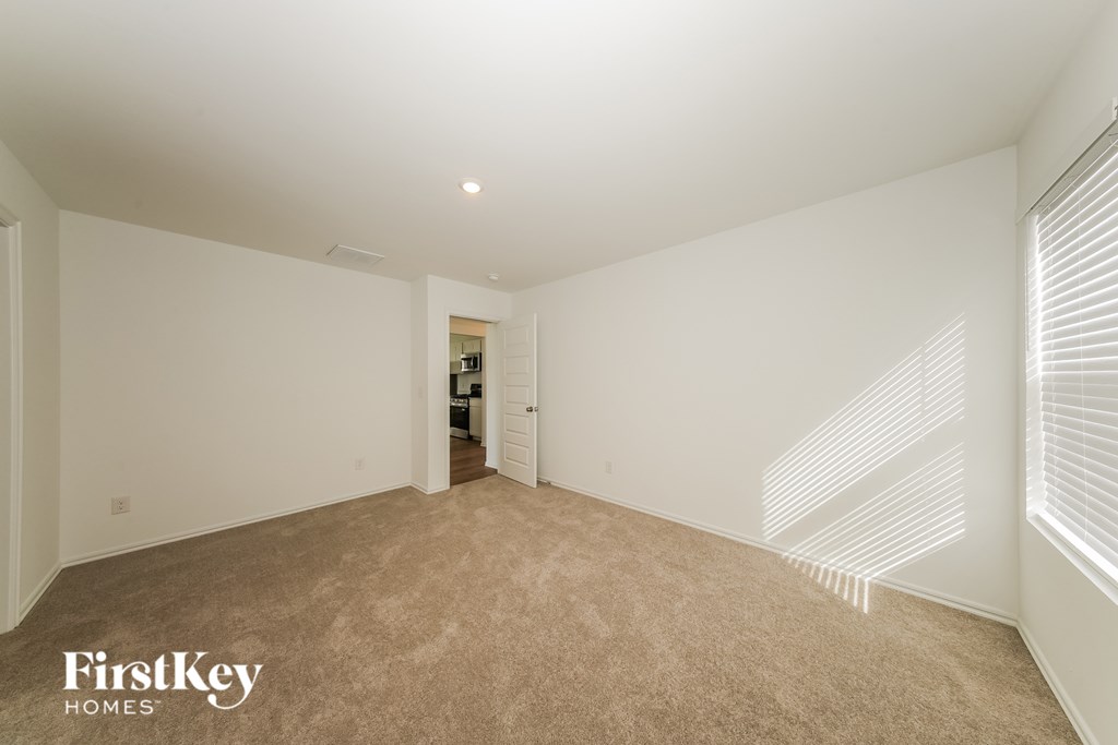 A spacious room with a carpeted floor and white walls, with a doorway leading to another room.