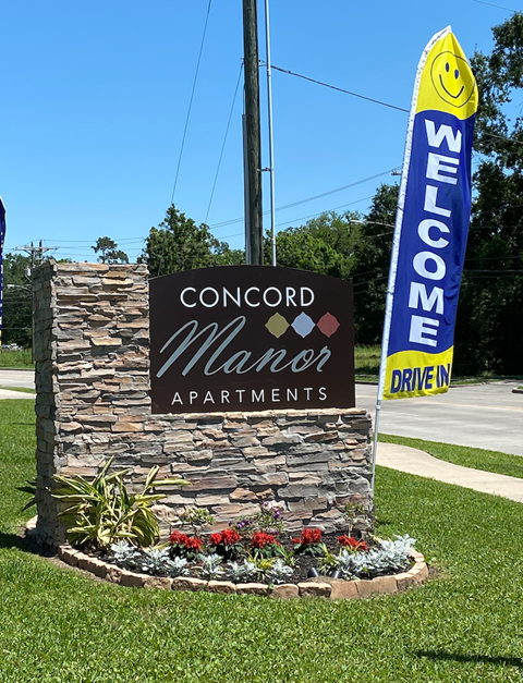 A welcome sign for Concord Manor Apartments is displayed in front of a stone wall.