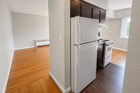 A white refrigerator is in the corner of a room with wood floors.