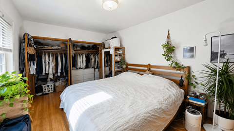 A bedroom with a large bed and a closet with clothes hanging.