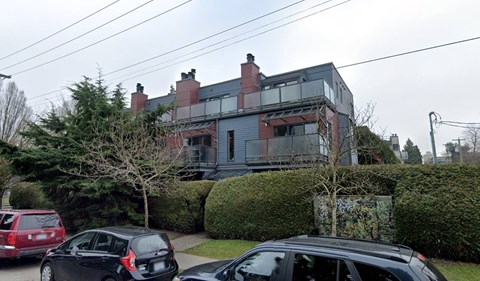 A black car is parked in front of a grey house with a tree on top of it.