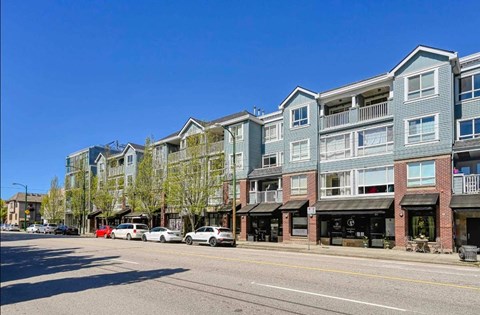 A row of apartment buildings line a street with cars parked on the side.