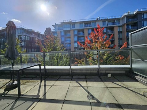 A balcony with a table and chairs overlooking a building and trees.