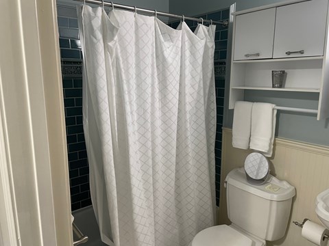 A white shower curtain with a diamond pattern hangs in a bathroom.