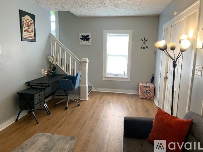 A living room with a couch, a chair, a desk, and a staircase.