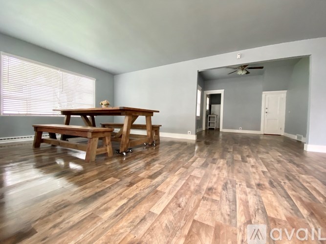 A room with a wooden table and bench, a ceiling fan, and a door leading to another room.