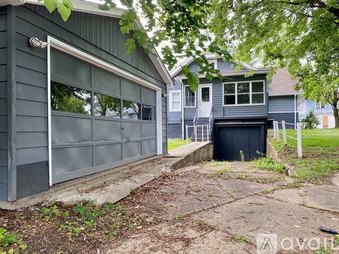 A grey house with a black trash bin in front.