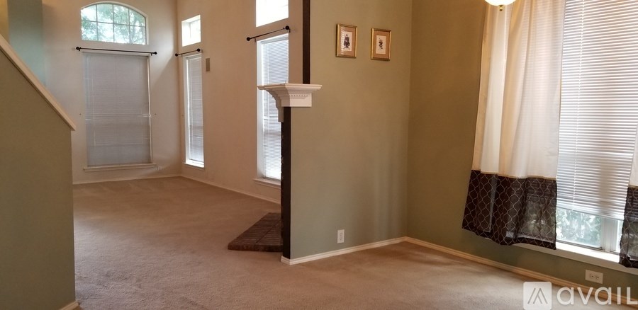 A room with a carpeted floor and a window with white curtains.