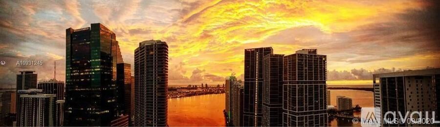 A city skyline at sunset with tall buildings and a body of water in the foreground.