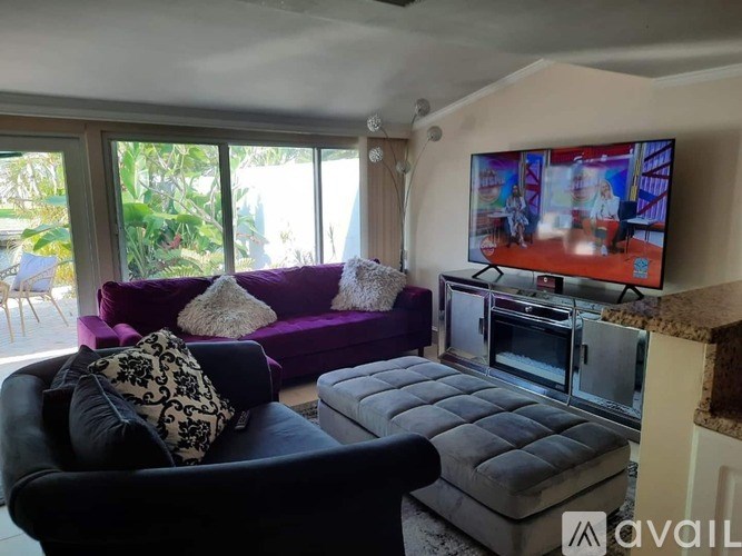 A living room with a purple couch and a television on the wall.