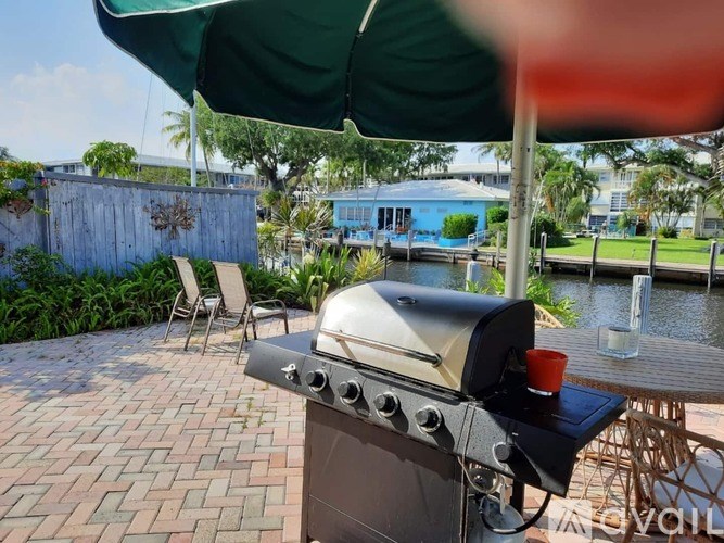 A barbecue grill is set up on a patio with a table and chairs under a green umbrella.