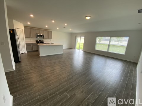 A spacious living room with hardwood floors and a kitchen area in the background.