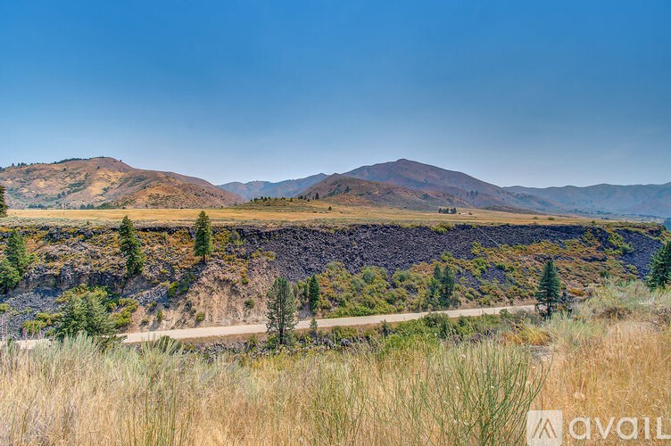 A landscape with a dirt road and trees in the foreground and mountains in the background.