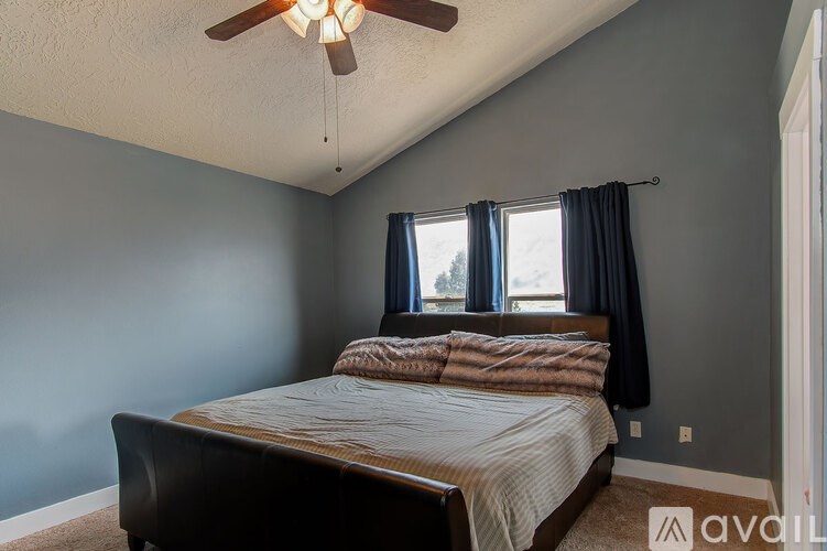 A bedroom with a bed, a ceiling fan, and a window with curtains.