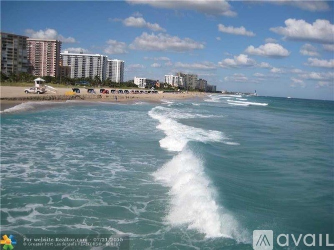 A beach scene with waves crashing onto the shore and buildings in the background.