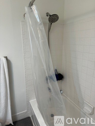 A white shower curtain hanging in a white tiled shower.