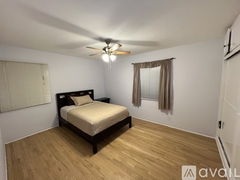 A bedroom with a bed, wooden floors, and a ceiling fan.