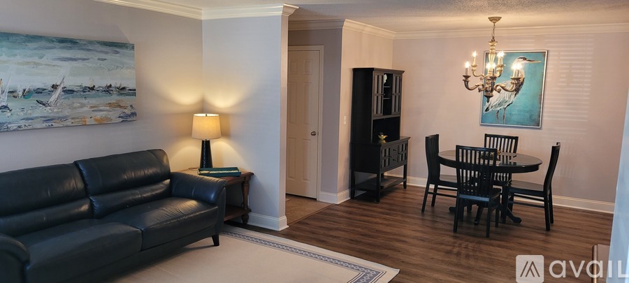 A living room with a black leather couch, a wooden dining table with chairs, a chandelier, and a painting on the wall.