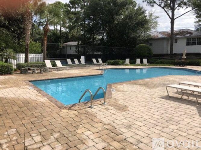 A pool with a brick patio and a white fence.