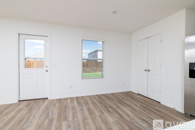 A room with wooden floors and white walls, with a window showing a view of a fence and a building.