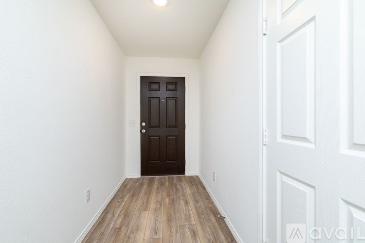 A hallway with a wooden floor and a dark brown door.