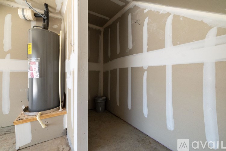 A room under construction with a water heater and a bucket of paint.