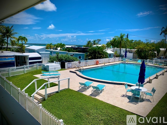 A pool with chairs and an umbrella is surrounded by a white fence.