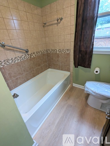 A bathroom with a tub, toilet, and a window with a brown curtain.