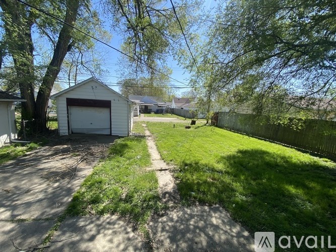A white garage is situated on a grassy area with a tree in front of it.