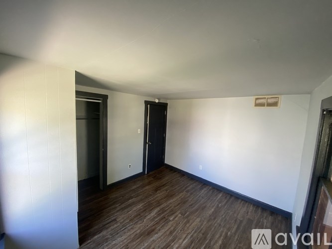 A room with wooden floors and white walls, with a door on the left and a small window on the right.