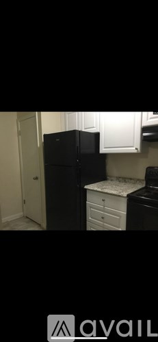 A black refrigerator in a kitchen with white cabinets.