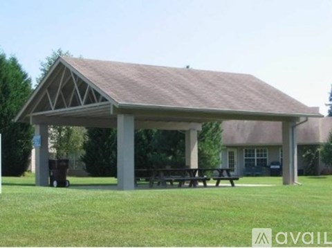A pavilion with a brown roof and a picnic table sits in a grassy area.