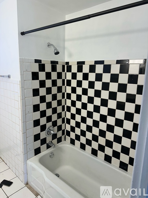A white bathtub sits under a black and white checkered wall.