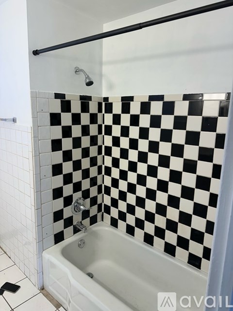 A white bathtub sits under a black and white checkered wall.