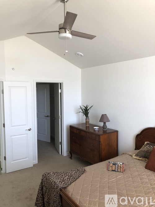 A bedroom with a bed, a nightstand with a plant, and a ceiling fan.