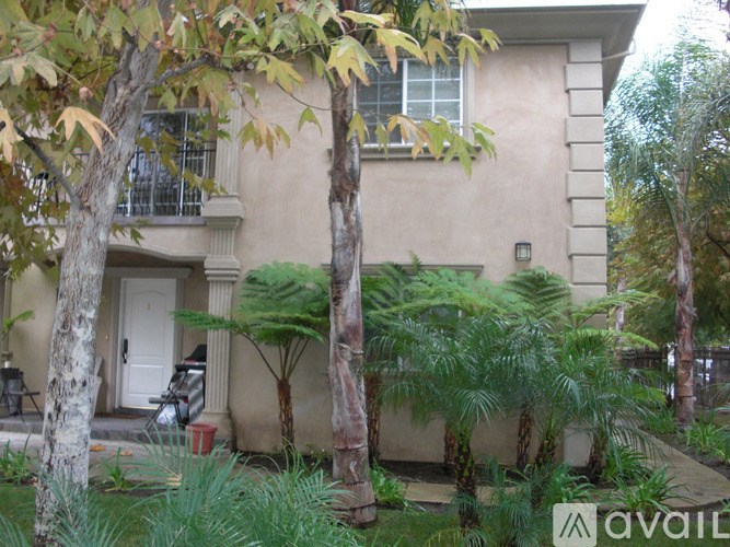 A beige house with a white door and a tree in front of it.