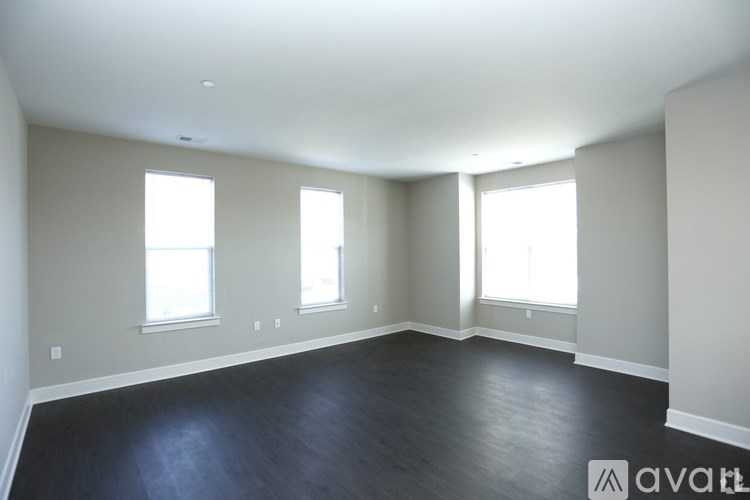 A large empty room with wooden floors and three windows.