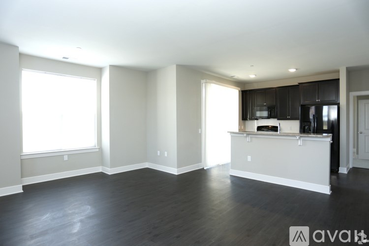 A spacious living room with hardwood floors and a kitchenette in the background.