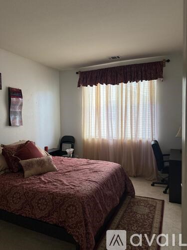 A bedroom with a bed, chair, and window with curtains.