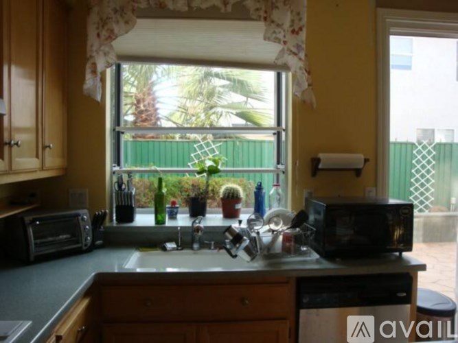 A kitchen with a sink, microwave, and window overlooking a green fence.