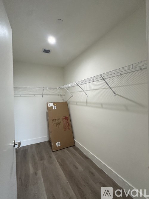 A cardboard box sits on the floor of a room with a shelf on the wall.